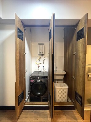 A compact, single-room bathroom with a built-in washer and dryer, a sink, and a small laundry basket.