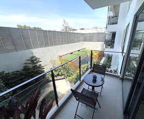 Een balkon met een glazen hekwerk, een tafeltje en twee stoelen.