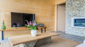 Un salon moderne avec un banc en bois, un socle en pierre, un téléviseur à écran plat fixé à un mur en bois et un mur en pierre intégrant un téléviseur.