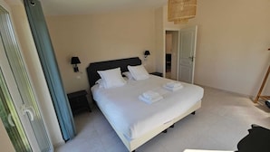 A bedroom with a bed, bedside tables, a hanging light fixture, and a door leading to another room. - Létendart (Saint-Quentin-en-Tourmont)