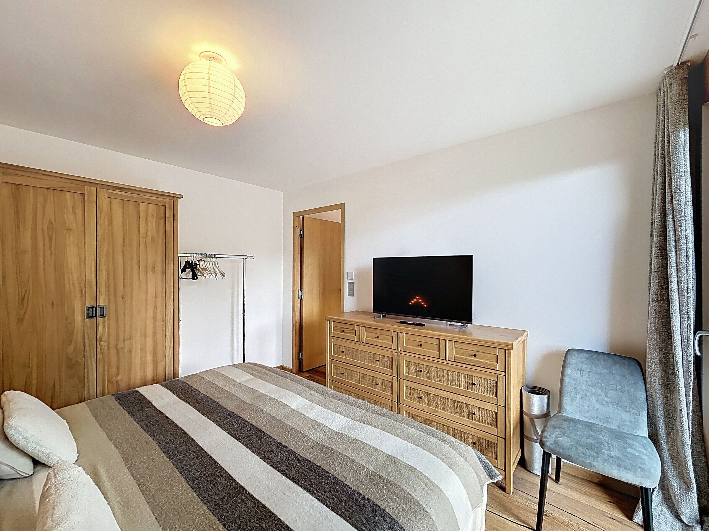 Ein Hotelzimmer mit einem großen Bett, einem Holzschrank, einem Fernseher auf einer Holzkommode und einem Sessel.