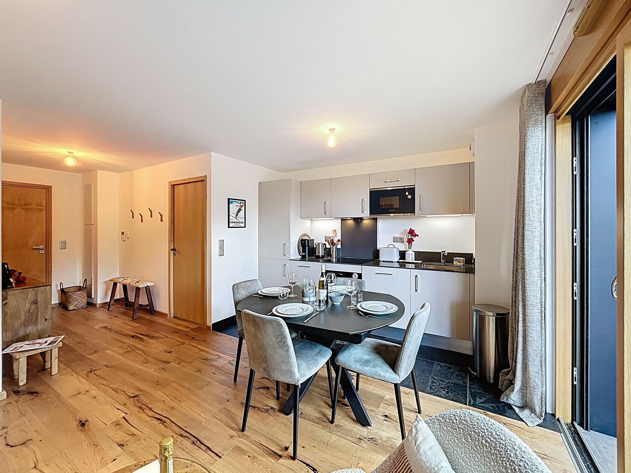 A modern kitchen with a dining area, wooden flooring, and a small table with chairs.