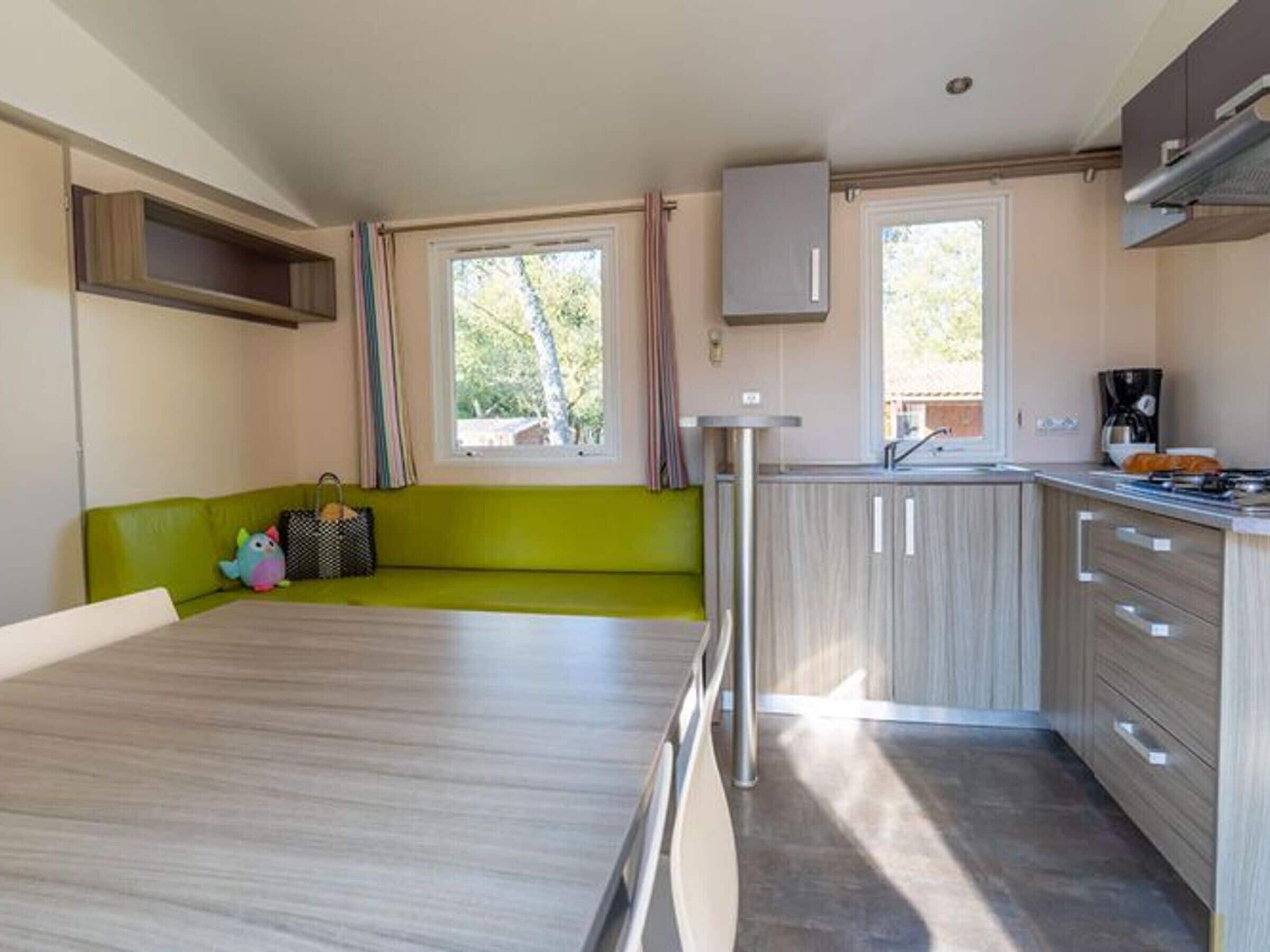 A compact kitchen with a green sofa, a dining table, and a coffee machine.