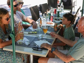 A group of people seated at an outdoor table with drinks and a laptop, suggesting a casual dining or meeting setting.