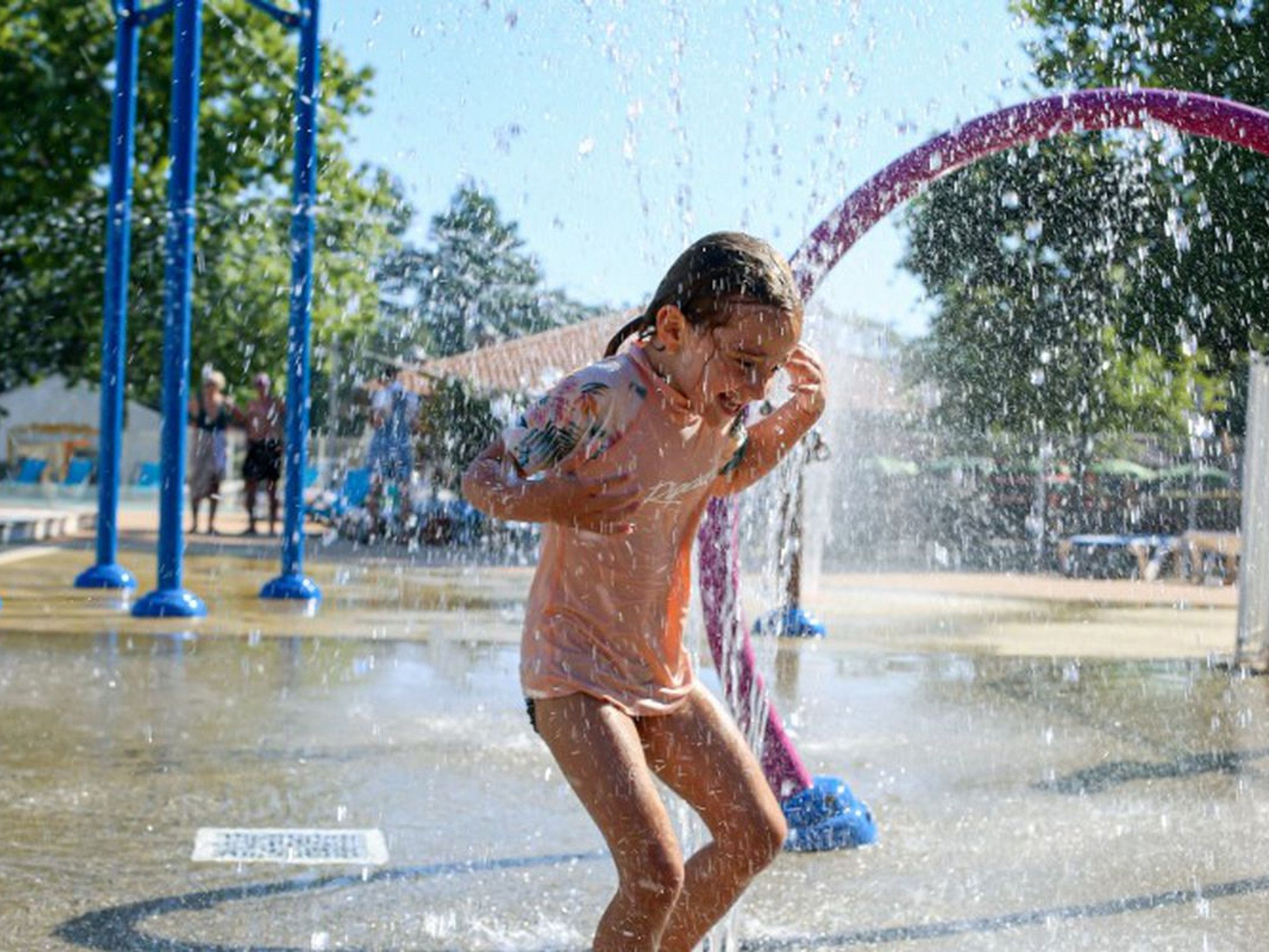 A person playing in a water park with water jets and a large arch structure.