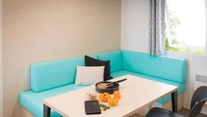 A teal sofa with a white table and black chairs in a room with a window and a radiator. - Mobile home with terrace in Saint-Gildas-de-Rhuys (Saint-Gildas-de-Rhuys)