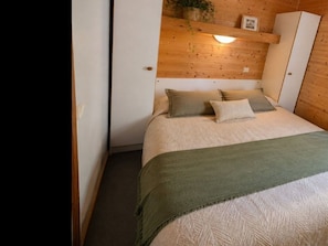 Une chambre à coucher avec un lit, des oreillers, une couverture verte, des murs en bois, une lampe fixée au mur et une plante.