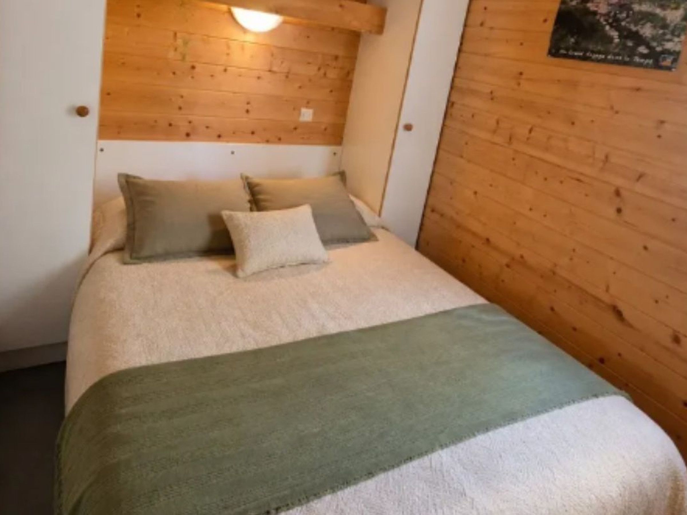 Een eenpersoonsbed met een deken in groen en wit, twee kussens, en een hoofdbord met een lamp.