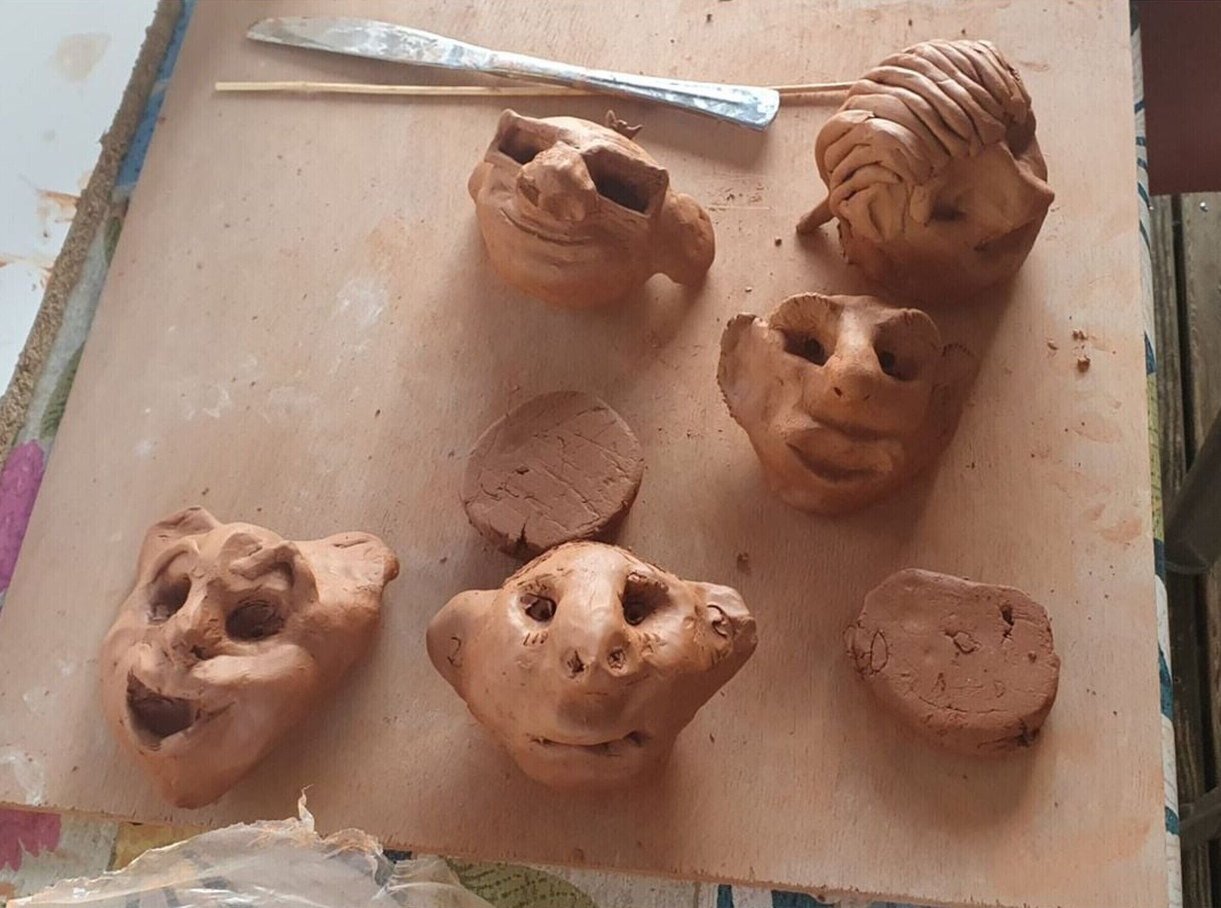 A clay sculpture with a sculpting tool on a work surface.
