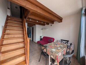 A wooden staircase leading to a room with a dining table covered in a patterned tablecloth, a red sofa, and a window with curtains.