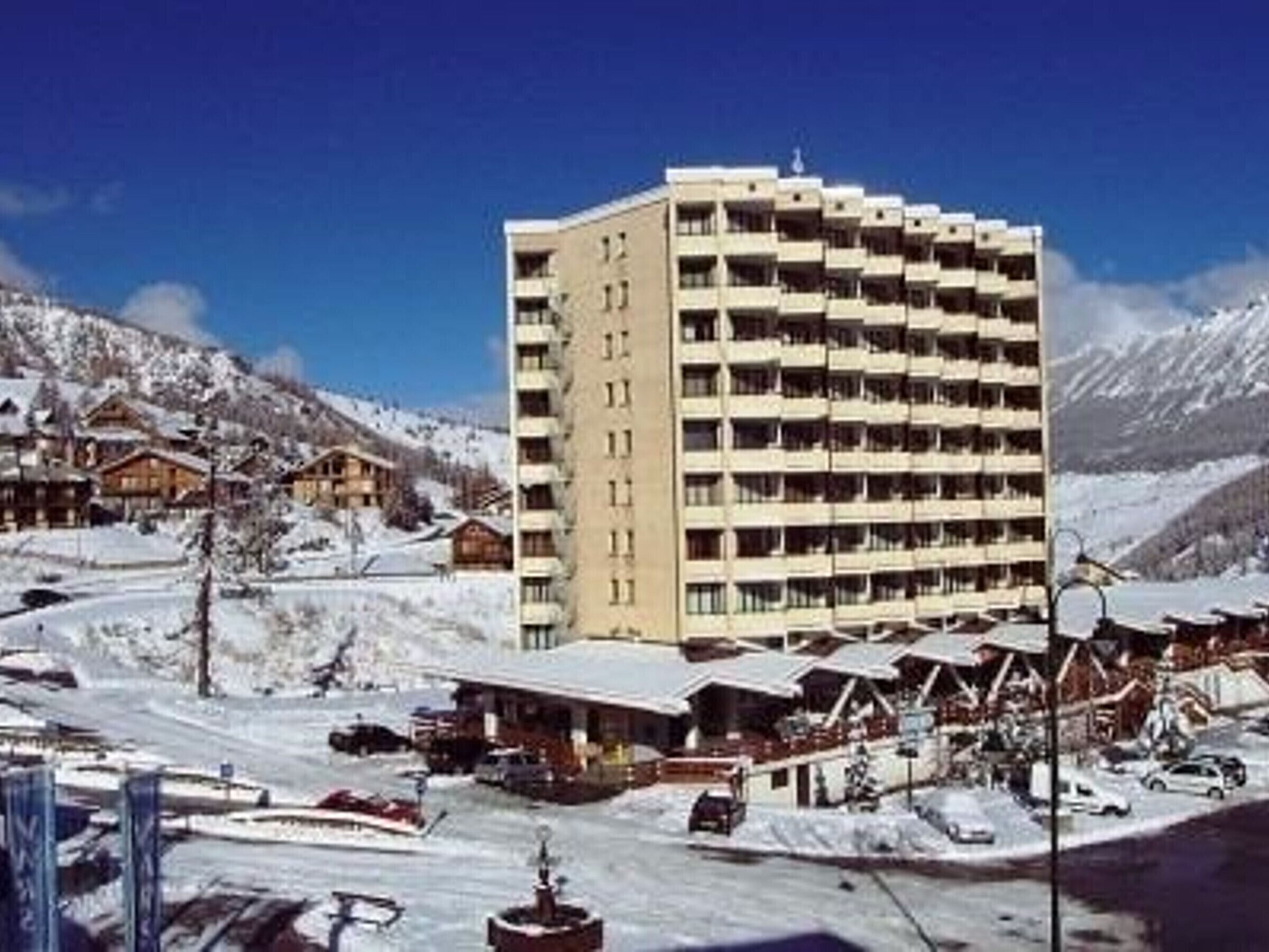Un grand hôtel doté de nombreux balcons, entouré de montagnes enneigées et situé à proximité d’une station de ski.