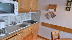 A kitchen with wooden cabinets, a microwave, a sink, and a stove. There are two heart-shaped oven mitts hanging on the wall.