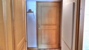 A narrow hallway with a wooden door at the end, a white wall, and a ceiling light.