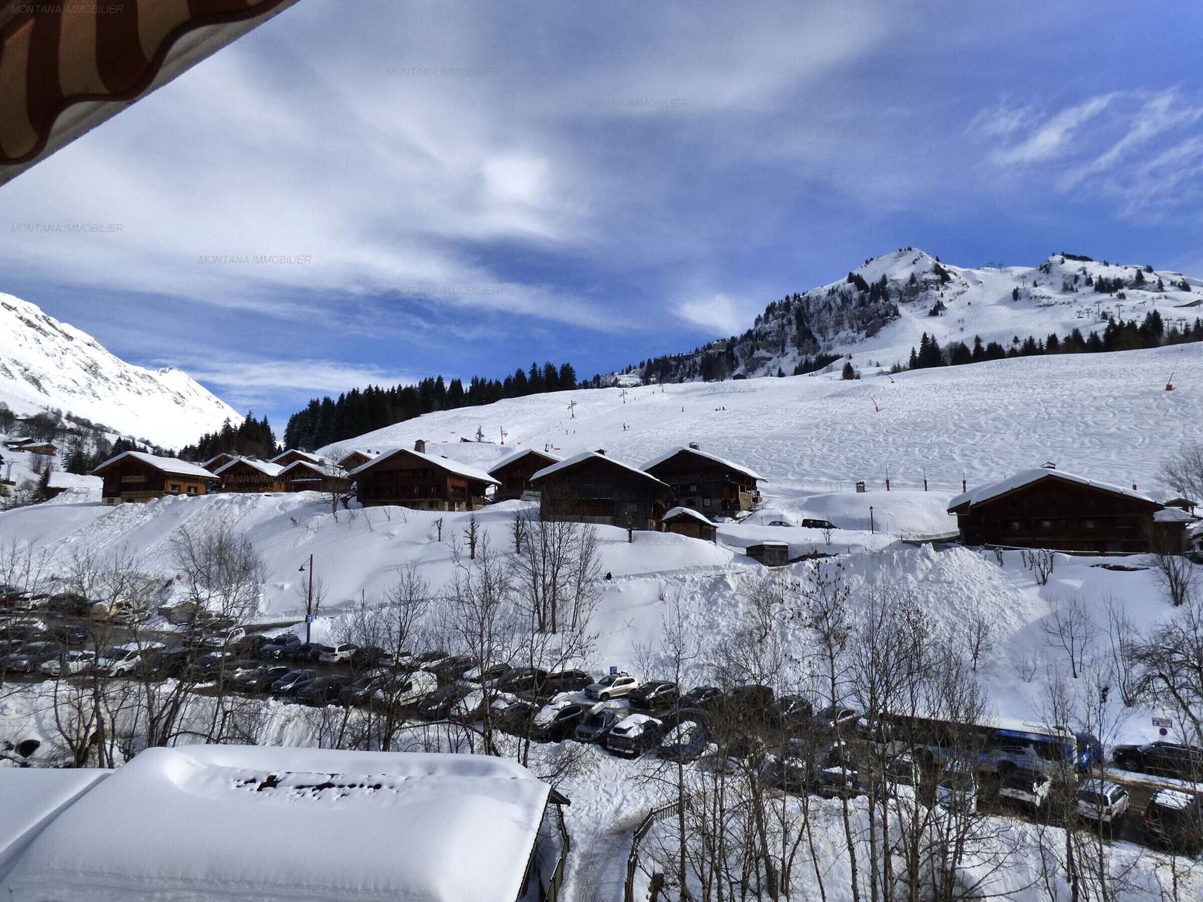 Ein verschneites Bergdorf mit Holzhütten, einer Skipiste und wolkenlosem, blauem Himmel.