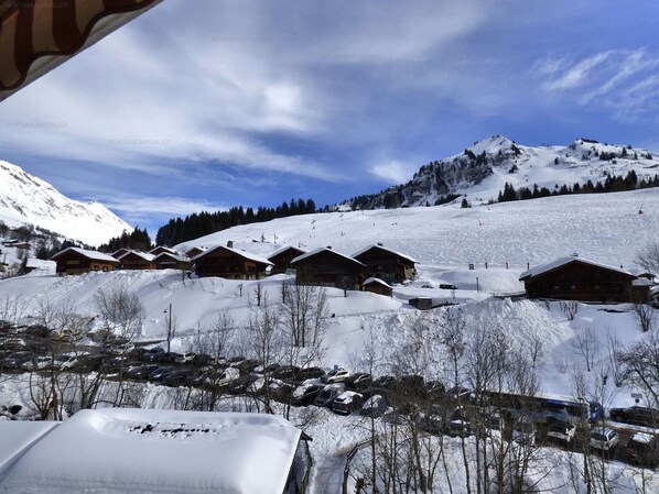 A snow-covered mountain village with wooden cabins, a ski slope, and a clear blue sky.