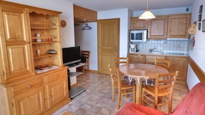 A compact kitchen with wooden cabinets, a microwave, and a dining table with chairs.