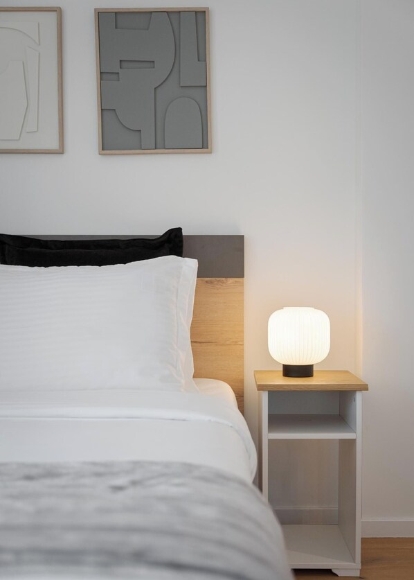 A neatly made bed with white linens, a wooden headboard, and a bedside table with a lamp.