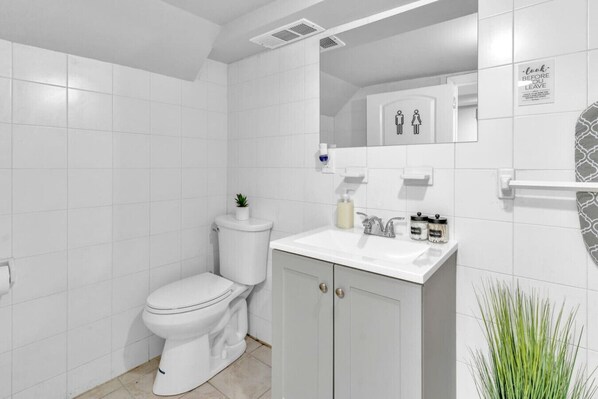 Une salle de bain moderne avec des toilettes, un lavabo et un miroir. Il y a un panneau sur le mur et une petite plante.