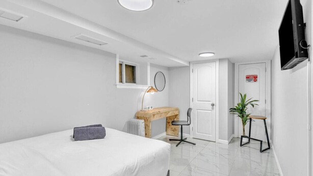 Habitación de hotel moderna y minimalista con cama, escritorio, silla, radiador, televisor y puerta con un letrero.