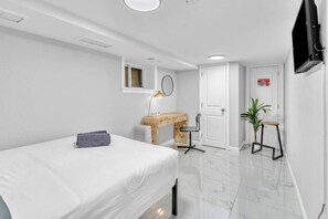 Une chambre d’hôtel moderne et minimaliste, équipée d’un lit, d’un bureau, d’une chaise, d’un radiateur, d’une télévision et d’une porte avec une pancarte.
