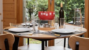 A dining table set with plates, glasses, cutlery, a red bowl, a bottle, and a pitcher, with a view of greenery outside. - Lovely apartment for 3 guests with WIFI, TV and terrace (Ovronnaz)