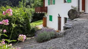 A house with a wooden balcony, a stone wall, and a gravel driveway. - Lovely apartment for 3 guests with WIFI, TV and terrace (Ovronnaz)