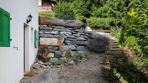 A stone pathway leading to a house with green shutters and a stone wall. - Lovely apartment for 3 guests with WIFI, TV and terrace (Ovronnaz)