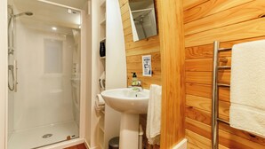 Un baño con ducha de vidrio, lavamanos blanco y pared de madera.