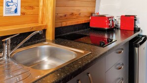 Una cocina con un lavamanos de acero inoxidable, paneles de pared de madera, un tostador rojo y un lavavajillas negro.