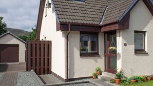 A two-story house with a sloped roof, a front door, and a small porch area with potted plants. - Beautiful  villa for 5 guests with WIFI and TV (Isle Of Skye)