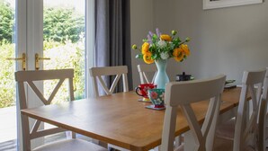 A dining area with a wooden table, white chairs, a vase with flowers, and a painting on the wall. - Beautiful  villa for 5 guests with WIFI and TV (Isle Of Skye)