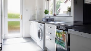 A modern kitchen with a washing machine, a window with plants, and a view of the outside. - Beautiful  villa for 5 guests with WIFI and TV (Isle Of Skye)