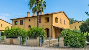 Eine gelbe Villa mit einer Palme, umgeben von viel Grün und einem verschlossenen Eingang.