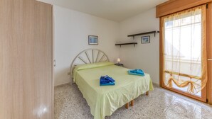 Ein Schlafzimmer mit einem Bett, einem Holzschrank, einem Nachttisch mit Lampe und einem Fenster mit Vorhängen.