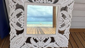 A white ornate picture frame with a view of a wooden pier and turquoise sea.