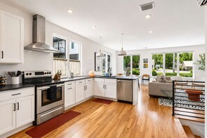Une cuisine moderne avec des meubles blancs, une hotte en acier inoxydable et une grande fenêtre.