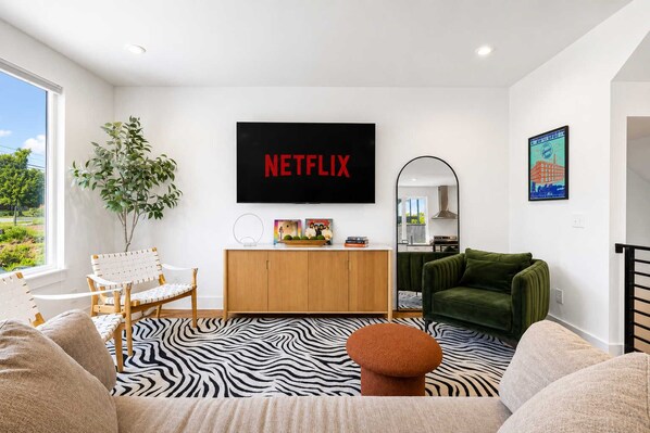 Un salon moderne avec un grand téléviseur à écran plat, un canapé vert, un tapis à motifs zébrés et un meuble en bois.