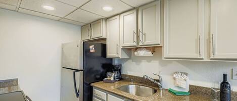 A kitchen with white cabinets, a stainless steel refrigerator, a coffee maker, a sink, and a wine bottle.