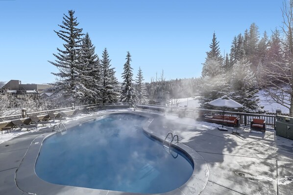 A heated outdoor swimming pool surrounded by snow-covered trees and a clear blue sky. - Slope-side Studio, Peak 9, Dog Friendly, Kitchen (Breckenridge)
