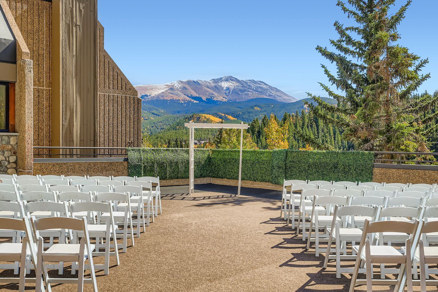 Un lieu de réception en plein air pour les mariages, doté d’un sol en gravier, de chaises blanches et offrant une vue sur les montagnes.