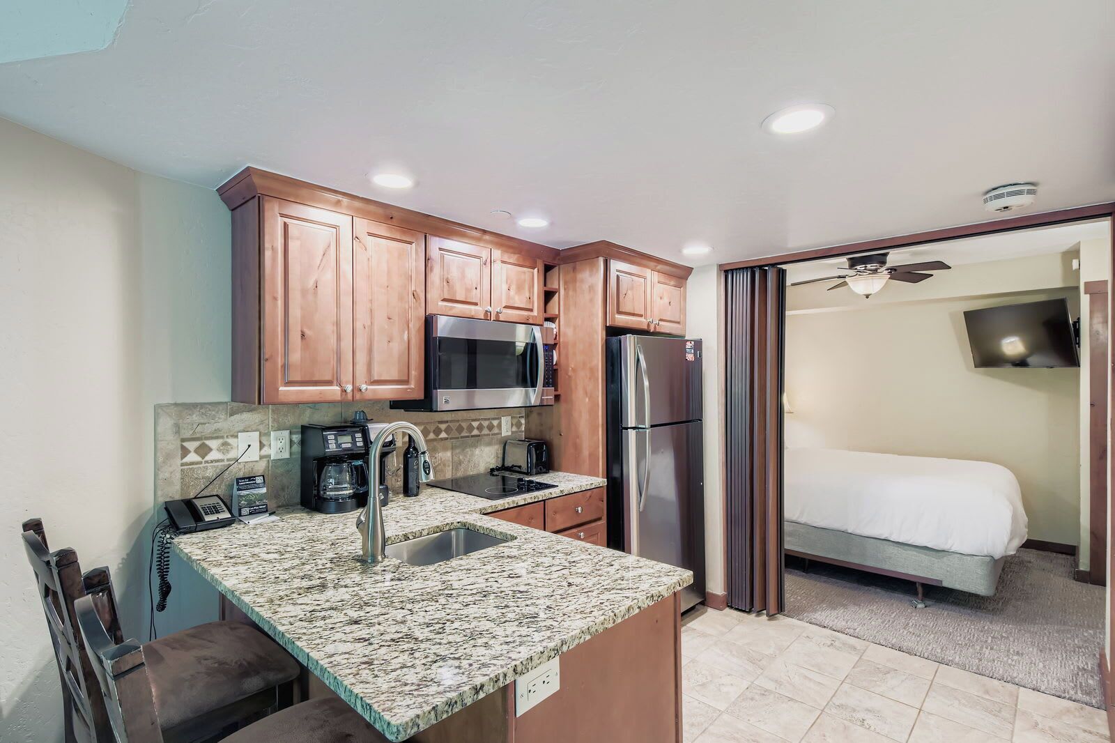 A compact kitchen with granite countertops, wooden cabinets, a microwave, a refrigerator, and a coffee maker.