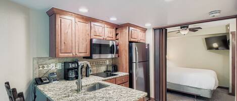 A compact kitchen with granite countertops, wooden cabinets, a microwave, a refrigerator, and a coffee maker.