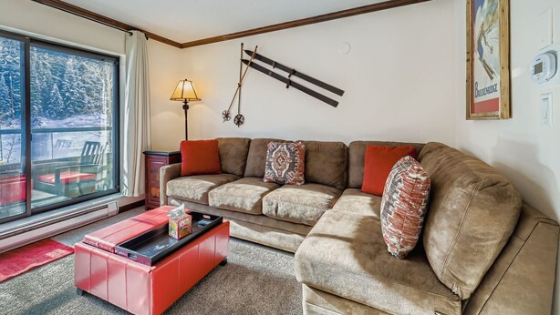 A cozy living room with a large window, a sofa with patterned cushions, a red coffee table, and a wall-mounted ski rack. - Ski In, Ski Out Studio, Peak 9 Views From Balcony, Hot Tubs, Beaver Run (Breckenridge)