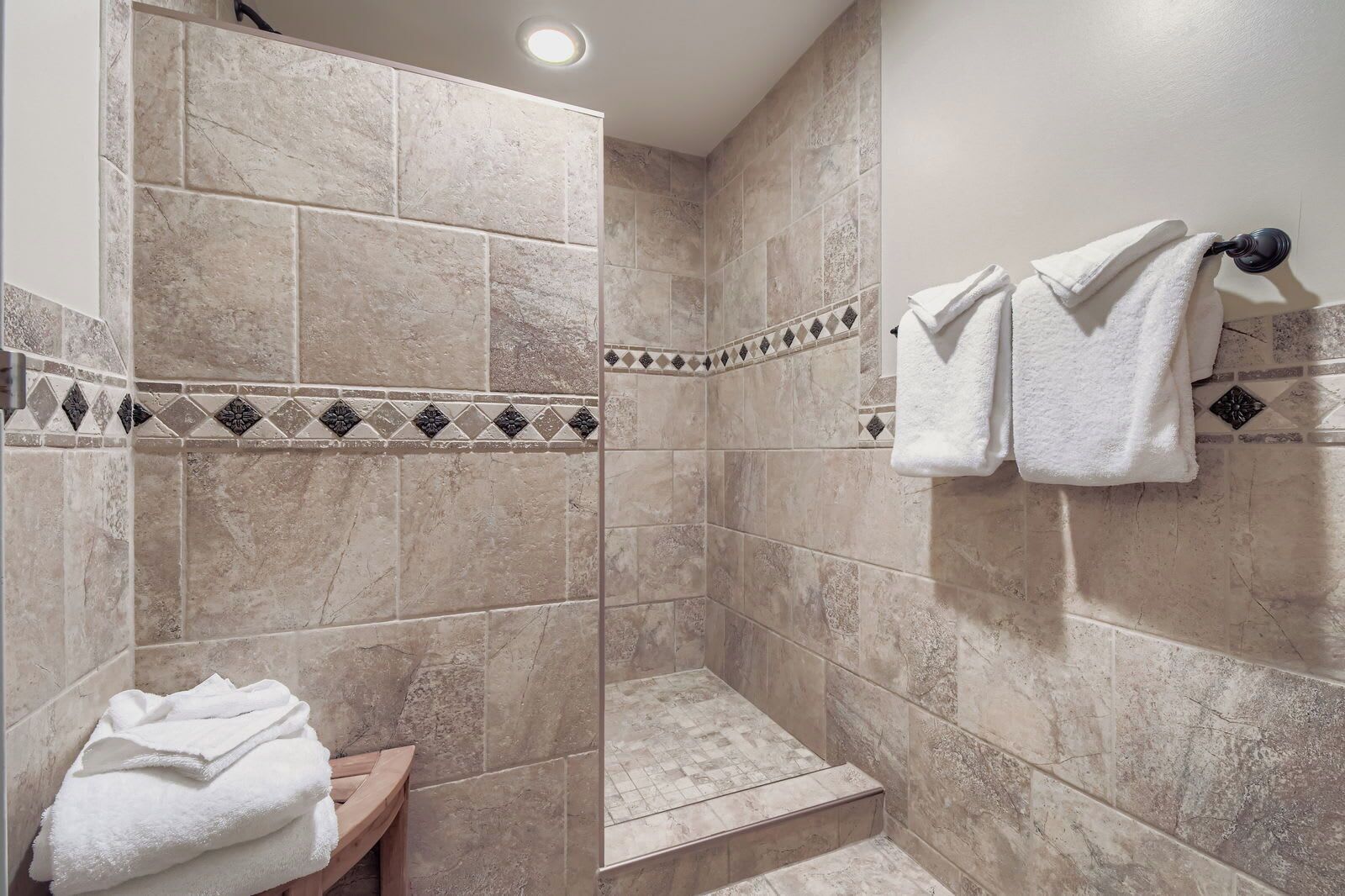 Un espace douche avec des carreaux de couleur beige, un petit banc en bois et un porte-serviettes avec deux serviettes.