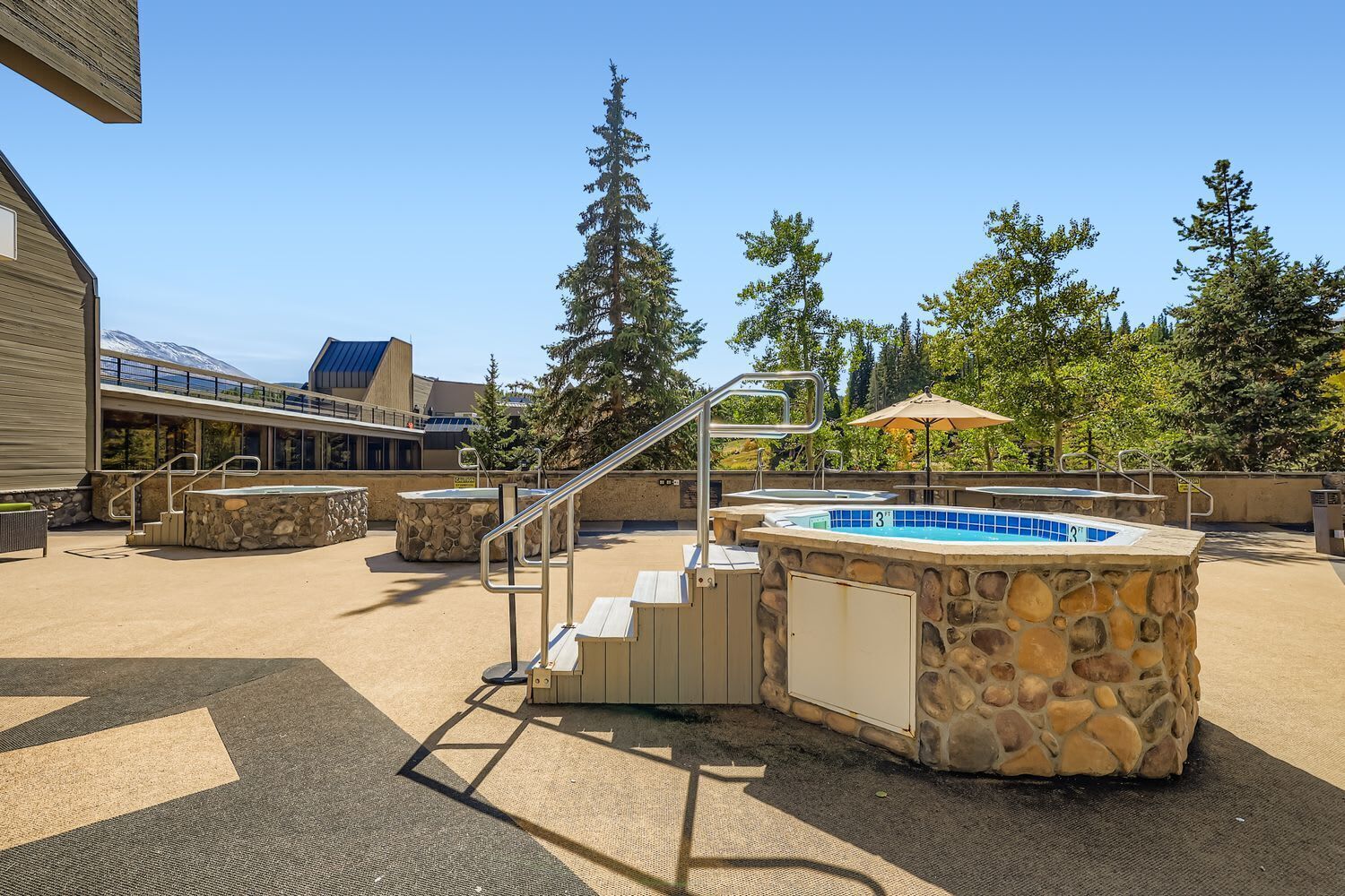 An outdoor swimming pool area with a stone wall, a hot tub, and a staircase leading to a covered deck.