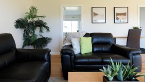 Una sala de estar con dos sofás de cuero negro, una planta verde grande y dos cuadros en la pared.