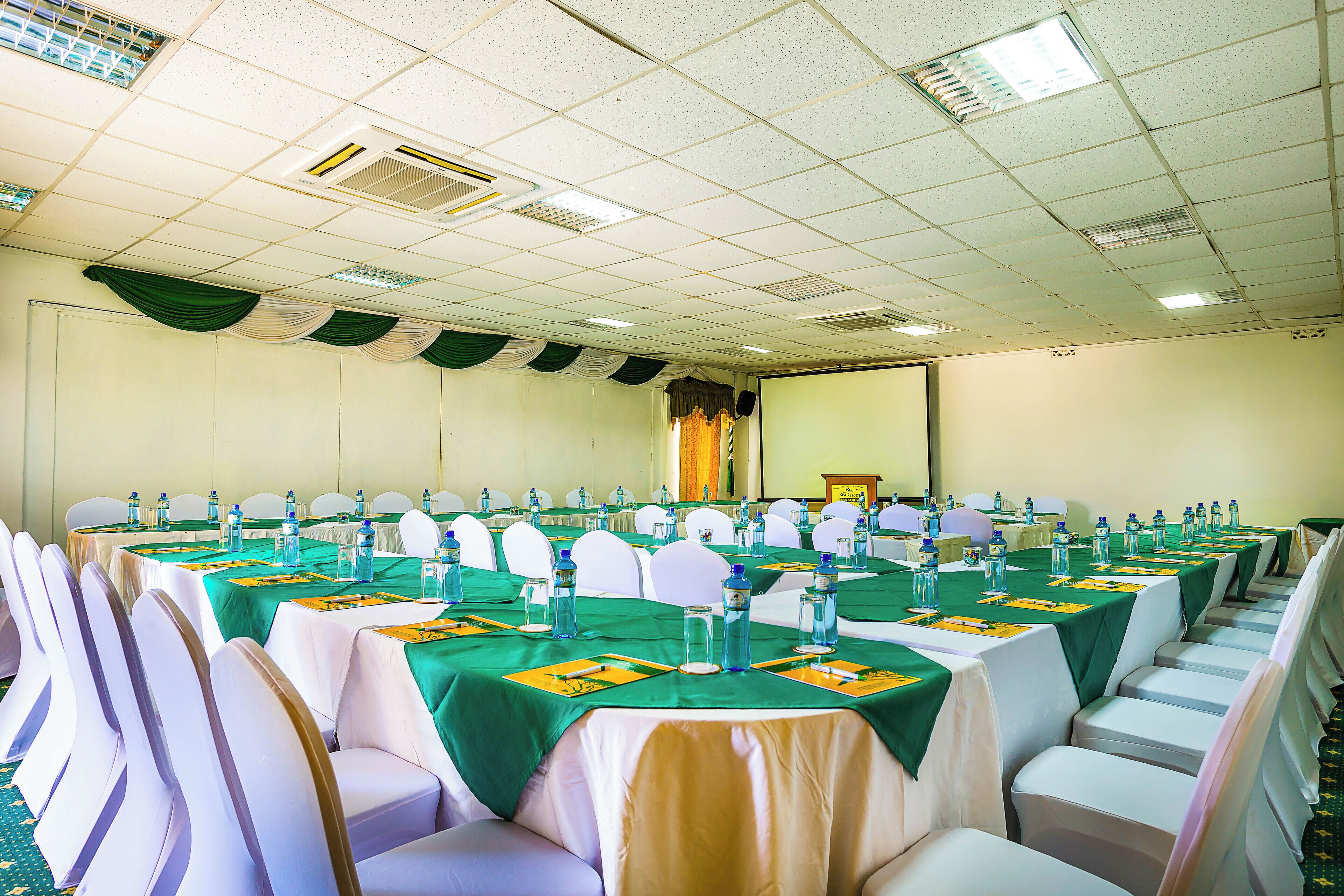 A conference room with long tables, chairs, and a projector screen.