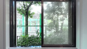 A window with a view of a green fence and trees.