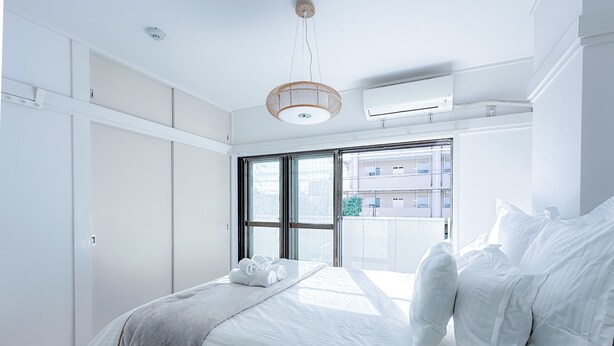 A modern bedroom with a large bed, white linens, a wooden headboard, a hanging light fixture, and an air conditioning unit.