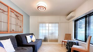 A modern living room with a sofa set, a dining table with chairs, a large window, and a decorative ceiling light.